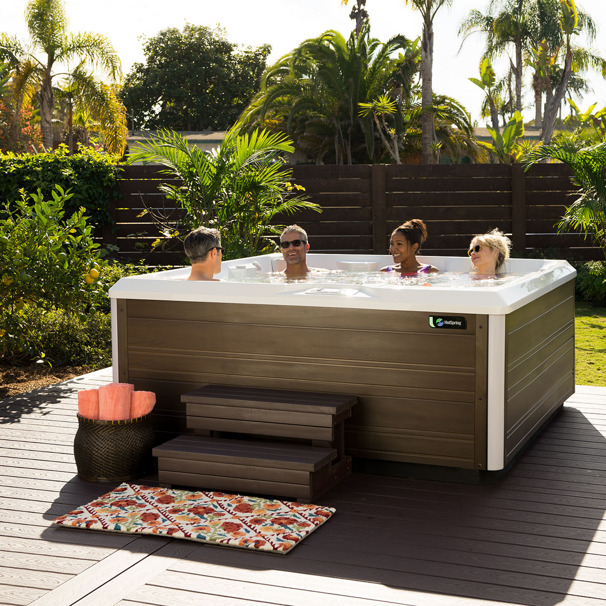 four people in a hot tub in the corner of a backyard