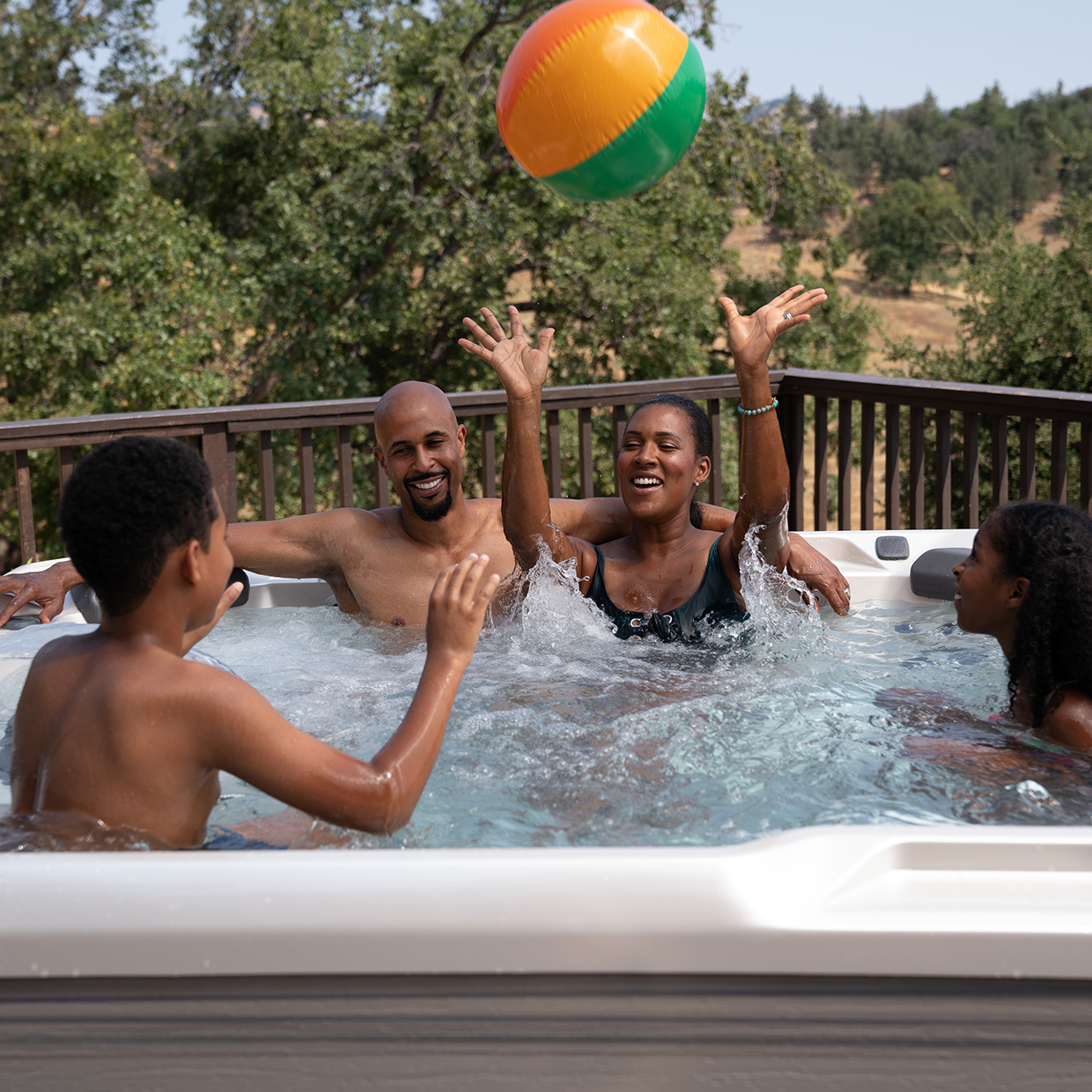 two parents and two kids in a hot tub throwing an inflatable ball